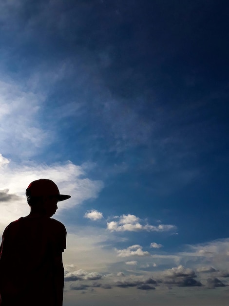 Foto silhueta de um menino de pé contra o céu azul