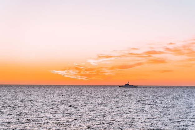 Silhueta de um navio no mar com uma linha de horizonte de sol laranja entre o céu e a água