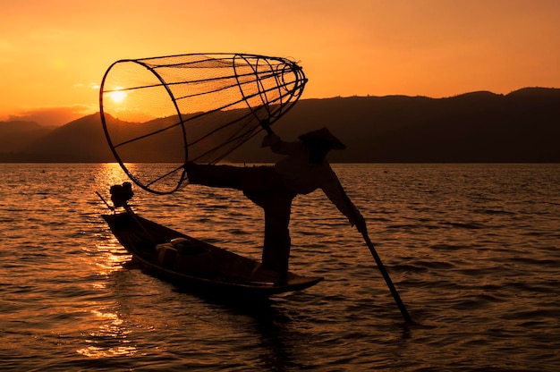 Silhueta de um pescador birmanês tradicional no Lago Inle ao pôr do sol em Mianmar