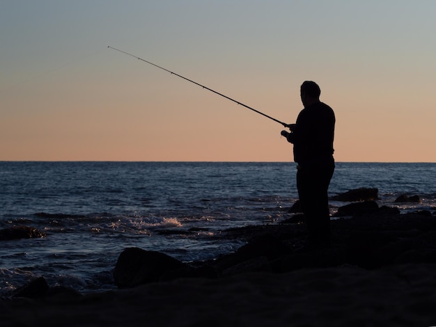 Silhueta de um pescador no fundo do mar e do céu após o pôr do sol