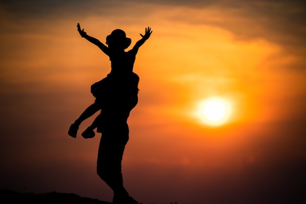 Foto silhueta de uma família com uma mãe feliz brincando com uma garota no céu do sol