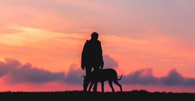 Silhueta de uma garota com um cachorro grande ao pôr do sol