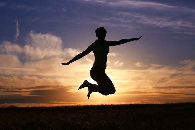 Silhueta de uma garota contra o céu pulando ao pôr do sol, conceito de felicidade