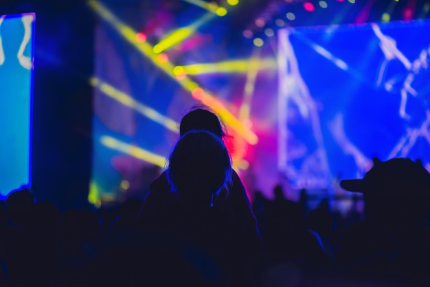 Silhueta de uma grande multidão em show contra um palco bem iluminado de show noturno de rock com