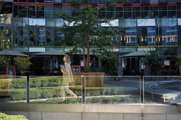 Foto silhueta de uma jovem empresária de terno bege andando no centro da cidade posando perto de prédios de escritórios
