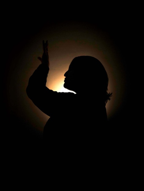 Foto silhueta de uma jovem mulher gordinha no escuro levantando a mão adivinhação para o amor