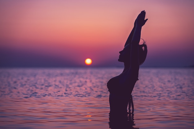 silhueta de uma jovem praticando ioga na praia ao nascer do sol