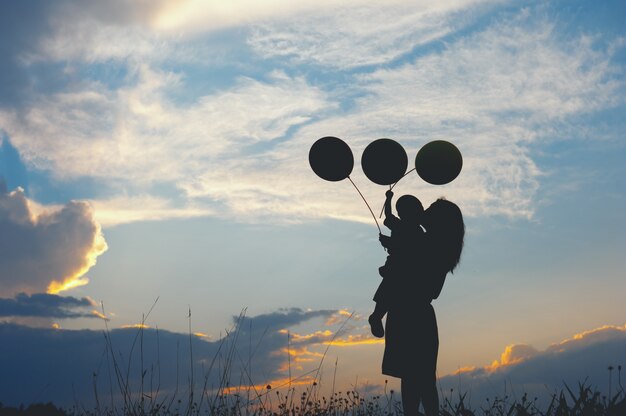 silhueta de uma mãe e filho brincando ao ar livre ao pôr do sol