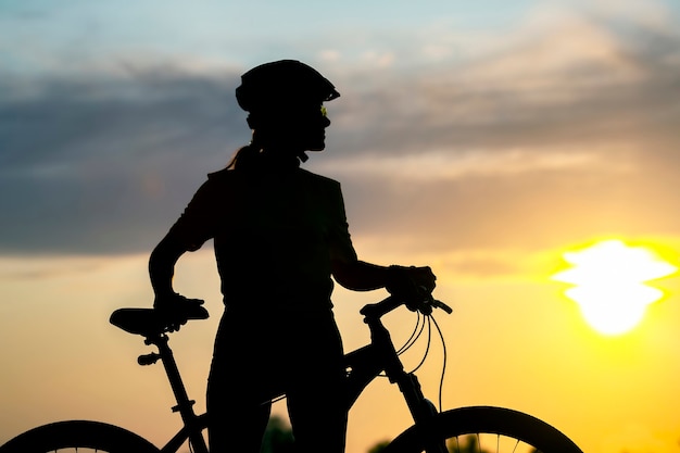 Foto silhueta de uma mulher ciclista em uma bicicleta no céu ao pôr do sol