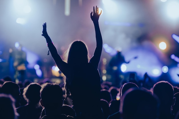 Silhueta de uma mulher com as mãos levantadas em um concerto