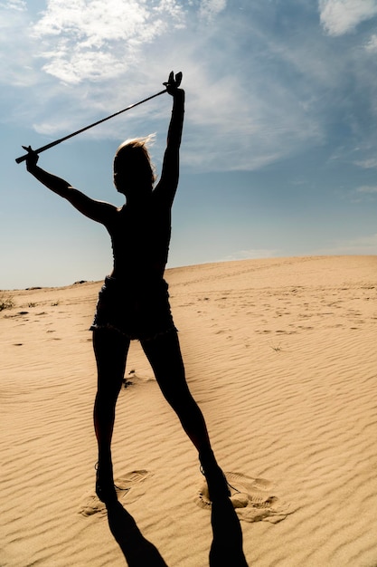 Silhueta de uma mulher com cabelo voador com taco de golfe no deserto