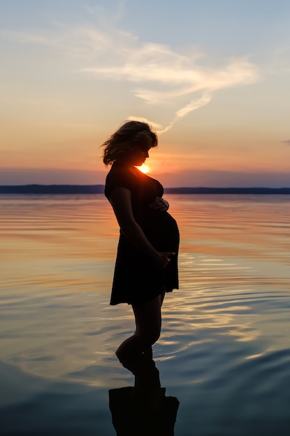 Silhueta de uma mulher esperando um bebê que está na água do lago