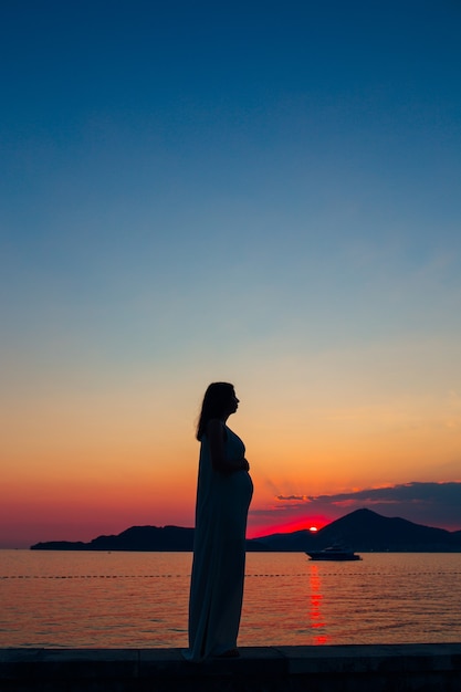 Silhueta de uma mulher grávida ao pôr do sol à beira-mar