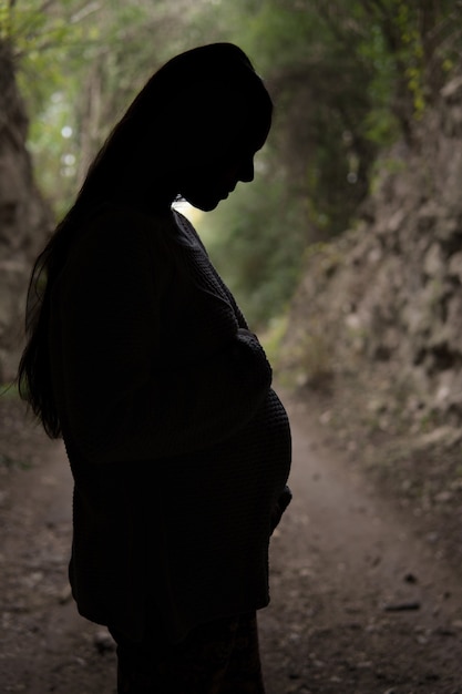 Silhueta de uma mulher grávida tocando e olhando para sua barriga.