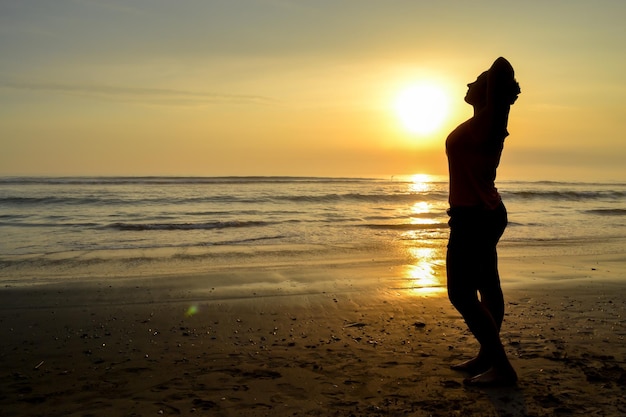 Silhueta de uma mulher posando sensualmente na costa de uma praia ao pôr do sol A hora de ouro