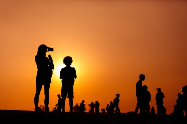 Foto silhueta de uma mulher segurando um smartphone tirando fotos com a criança e as pessoas da multidão