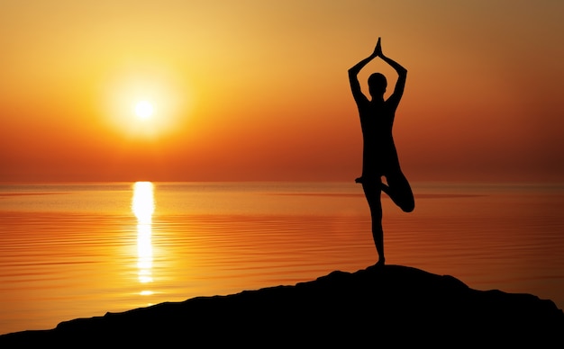 Silhueta de uma mulher yoga à noite. mulher fazendo ioga ao pôr do sol