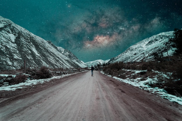 Silhueta de uma pessoa caminhando por uma estrada rural no meio das colinas nevadas à noite