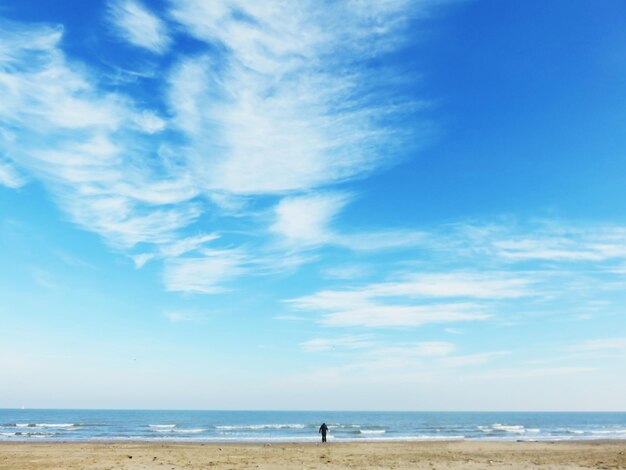 Foto silhueta de uma pessoa de pé na praia contra um céu nublado