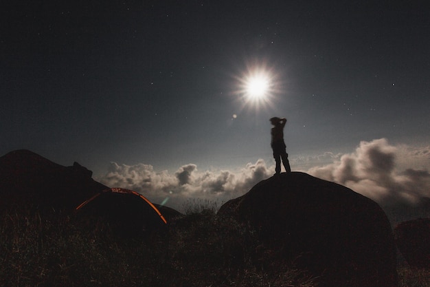 Foto silhueta de uma pessoa de pé no campo contra o sol brilhante