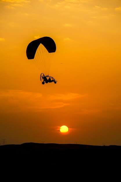 Silhueta de uma pessoa em parapente contra o céu laranja