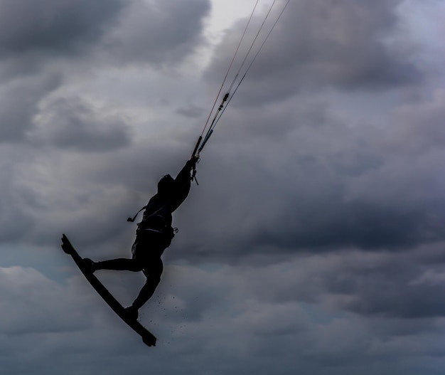 Silhueta de uma pessoa fazendo kiteboard contra um céu nublado ao anoitecer