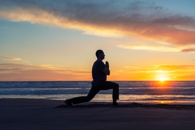 Silhueta de uma pessoa na praia fazendo ioga ou exercício ao pôr do sol