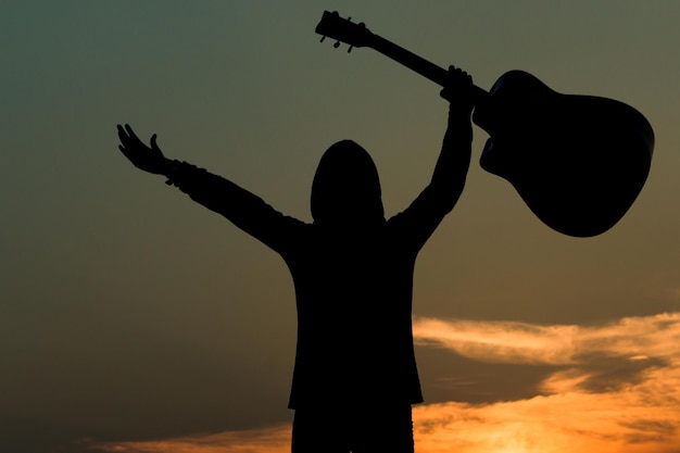 Silhueta de uma pessoa segurando uma guitarra contra o céu durante o pôr do sol