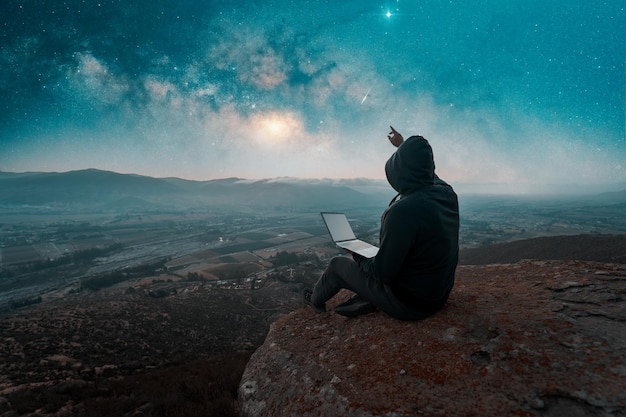 silhueta de uma pessoa sentada no topo da montanha com um laptop olhando para o céu com via láctea e fundo de estrelas