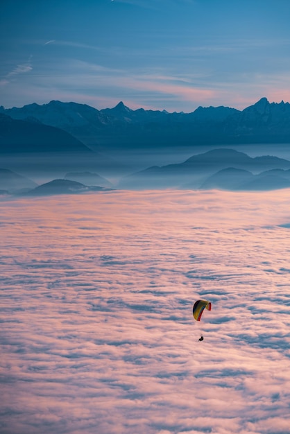 Silhueta de uma pessoa voando em parapente sobre uma paisagem nublada