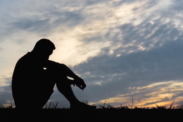 Foto silhueta de uma sessão de homem com tão triste por do sol.