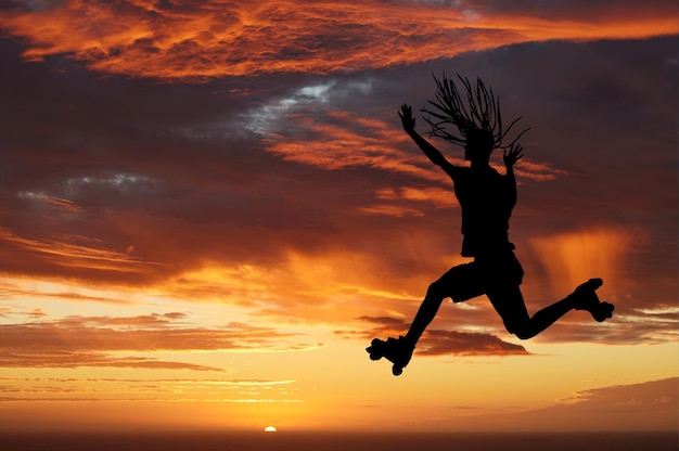 Foto silhueta do céu do sol e mulher de patins pulando contra um horizonte laranja enquanto desfruta de viagens de liberdade e diversão enquanto patina cenário de energia e beleza da natureza enquanto sai em uma aventura