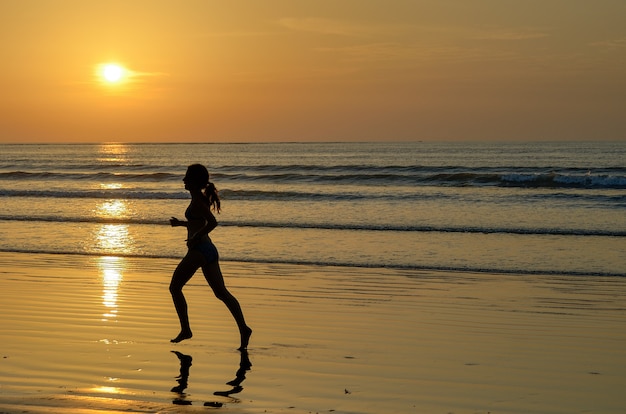 Silhueta do corredor de mulher correndo na praia do sol, fitness e conceito de vida saudável