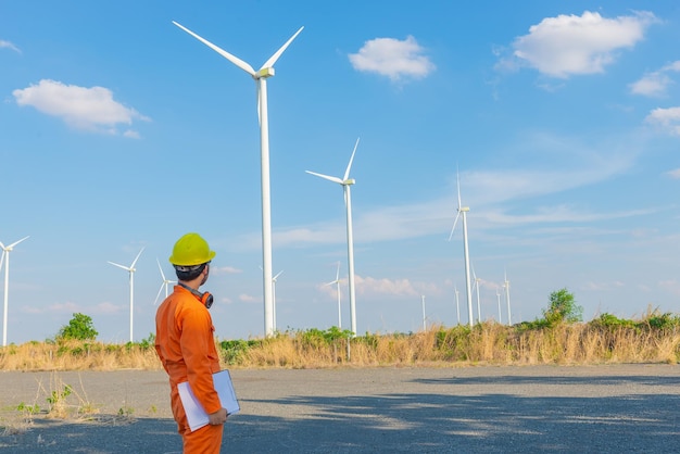 Silhueta do engenheiro homem trabalhando e segurando o relatório na estação geradora de energia da fazenda de turbinas eólicas na montanhaTailândia