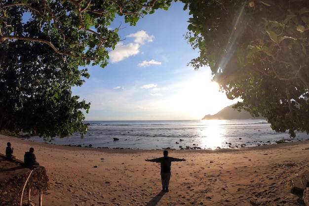 Foto silhueta do homem apreciando o pôr do sol na praia durante as férias de verão