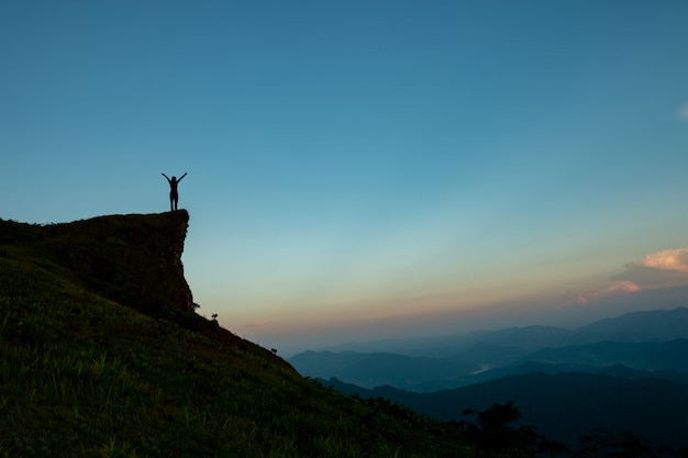 Silhueta do homem no topo da montanha sobre o céu e o sol luz de fundo