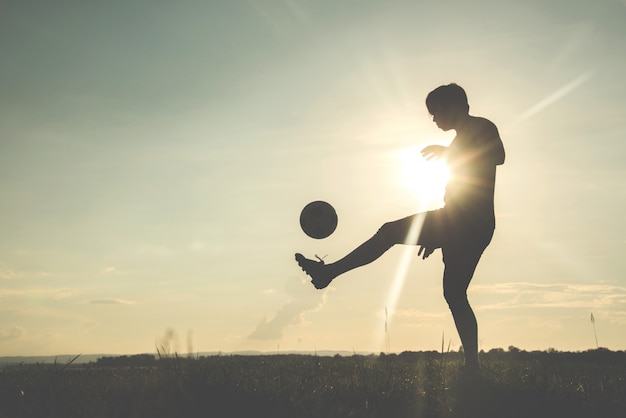 Silhueta do jogador de futebol com um soccerball contra o fundo do por do sol.