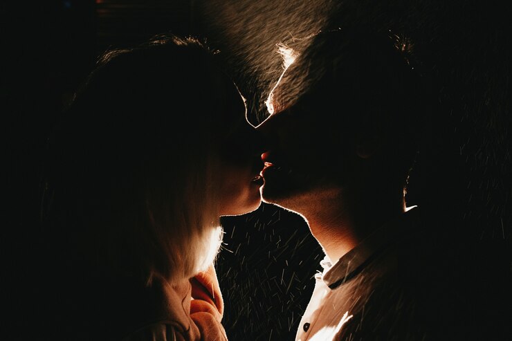 Silhueta do jovem casal feliz no amor beijando na noite sob chuva.