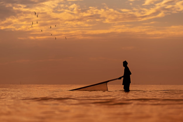 Foto silhueta do pescador local que encontra camarão usando redes tradicionais ao nascer do sol.