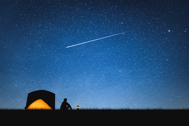 Silhueta do viajante que acampa na montanha e no céu noturno com estrelas. fundo do espaço.