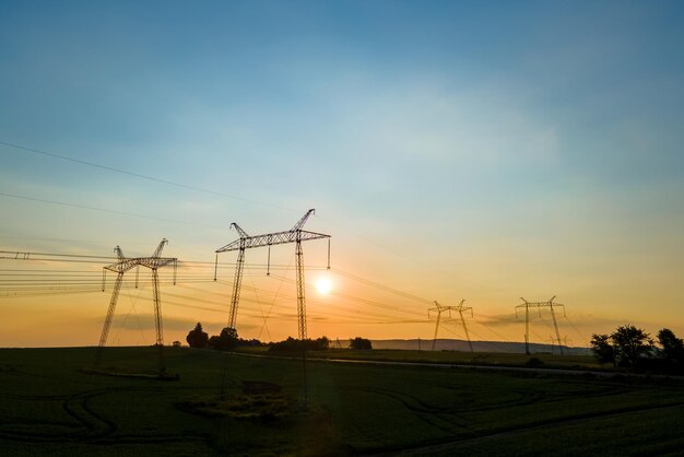 Silhueta escura de torres de alta tensão com linhas de energia elétrica ao nascer do sol.