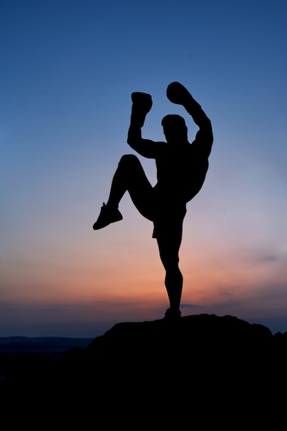 Silhueta escura de um boxer masculino musculoso ao ar livre no pôr do sol