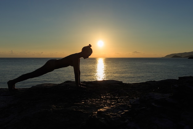 Silhueta feminina jovem fazendo exercícios de prancha em uma praia ao nascer do sol