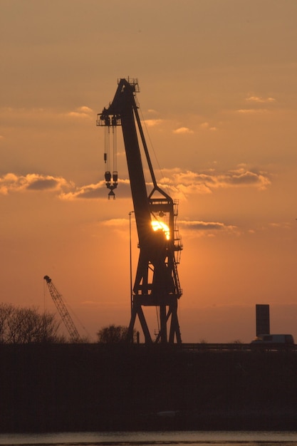 Foto silhueta de una grúa en el sitio de construcción contra el cielo durante el atardecer que se refleja