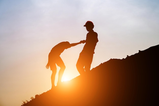 Silhueta de un hombre dando la mano a un hombre en la montaña contra el cielo durante la puesta de sol