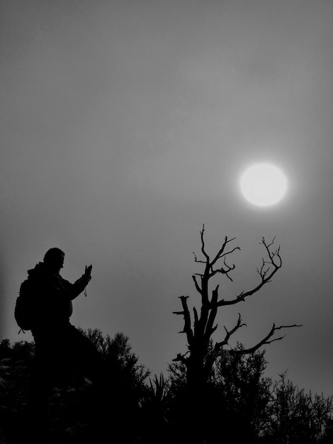 Foto silhueta de un hombre junto a un árbol desnudo contra el cielo