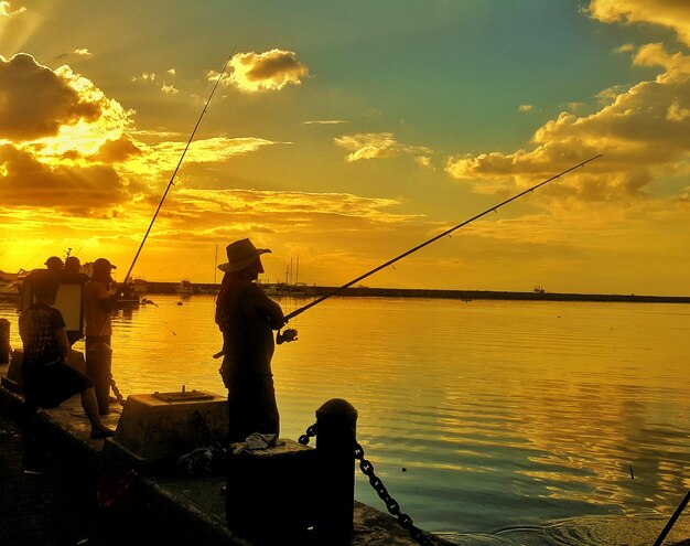 Foto silhueta de un hombre pescando en el mar contra el cielo al atardecer