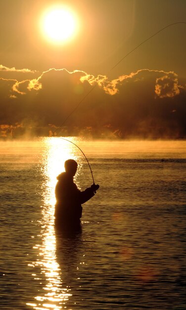 Foto silhueta de un hombre pescando en el mar contra el cielo durante la puesta de sol