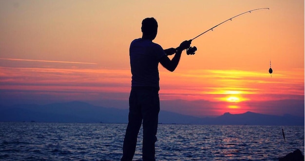 Silhueta de un hombre pescando en el mar contra el cielo durante la puesta de sol