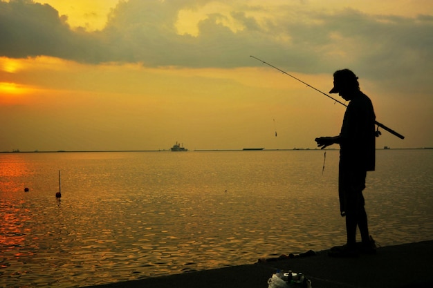 Silhueta de un hombre pescando en la playa durante la puesta de sol